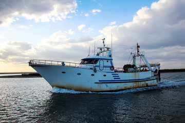 Naklejka premium Fishing boat returnig to coast at sunset in Huelva, Andalusia, Spain