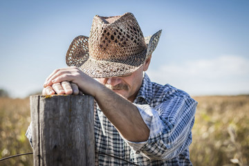 horizontal close up image of a caucasian cowboy praying by a fence post on a warm fall day.