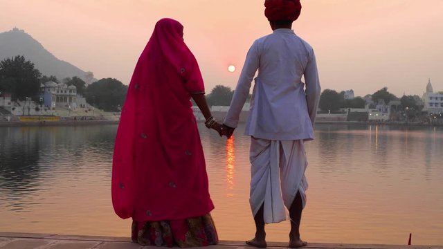 Romantic Indian couple in traditional dress watching the sun go down on Pushkar lake