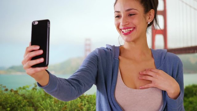 A Hispanic woman takes a selfie near the Golden Gate Bridge