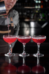 barman s hand with shake mixer pouring cocktail into glasses