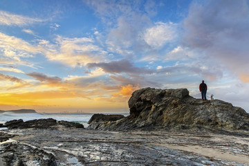 Unidentified man and his dog watching the sunset on a rock at Currumbin Rock, Gold Coast