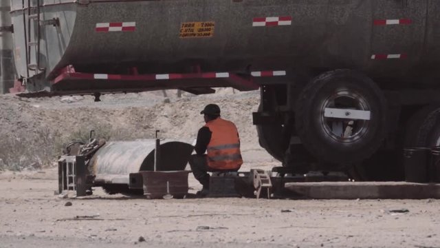 Construction worker resting under huge truck of fuel on a hot day