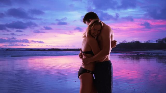 Two millennials in love hugging at the beach during the sunset