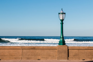 Lamppost on the Mission Beach boardwalk in San Diego, California with ocean waves in the background.