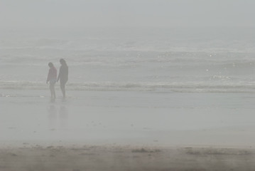 Sisters walk near waves through ocean mist