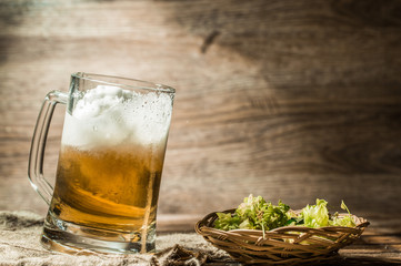 Frothy beer poured from cup on empty wooden background
