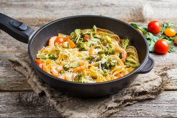 Pasta linguine with shrimps and broccoli in dripping pan on wooden background.