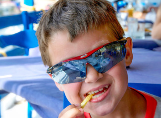 Naklejka premium caucasian little boy with sunglasses eating unhealthy potatoes