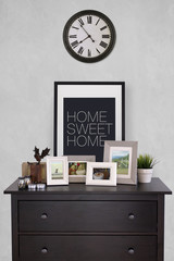 Picture frames collages on wooden cabinet with vintage clock in cozy living room, cement wall background