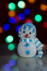 Illuminated snowman doll in front of Christmas tree lights, blurred background. Festive snowman...