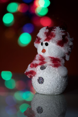 Illuminated snowman doll in front of Christmas tree lights, blurred background. Festive snowman with Christmas light background.