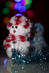 Illuminated two Snowman dolls in front of Christmas tree lights, blurred background. Festive...