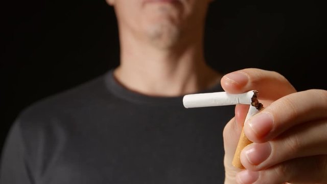 Young adult man holds a cigarette at one hand and then break it