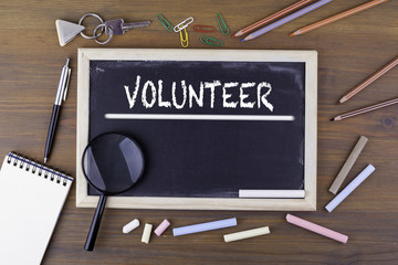 Volunteer. Text on the chalk board. Wooden table with a magnifying glass and writing utensils.