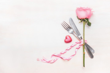 Table place setting : rose flower, cutlery and ribbon on light background, top view, place for text