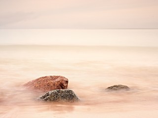 Long exposure of sea and big boulders sticking up from water within twilight time.