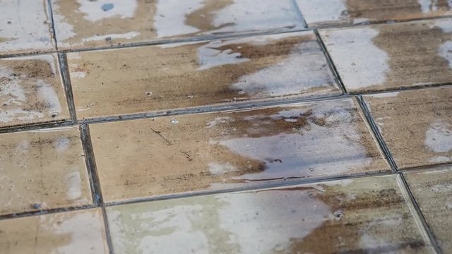 Raindrops fall on the flagstone sidewalk. The reflection of the sky and the blurry silhouettes on the wet surface. Wet sidewalk in the rain