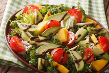 gourmet salad of mango, avocado, kiwi, lettuce, tomato dressed with balsamic sauce close-up. horizontal