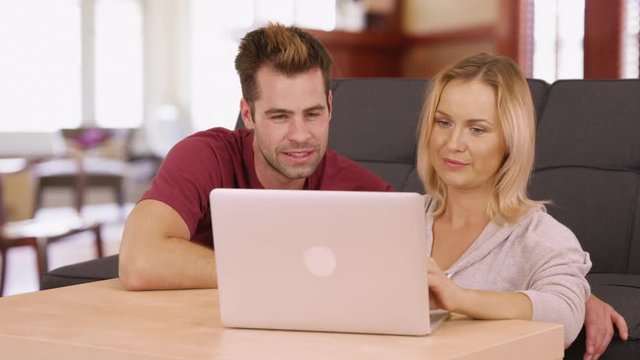 Cute millennial couple using laptop computer together at home in living room