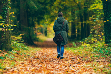 Fototapeta premium Woman with shoulder bag walking on path in autumn forest.