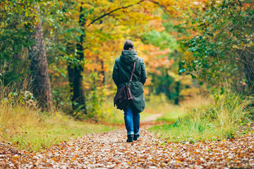 Fototapeta premium Woman with shoulder bag walking on path in autumn forest.