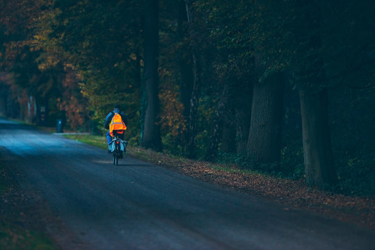 Fototapeta Biker with safety vest on road in autumn forest at dusk. Exel. Achterhoek. Gelderland.
