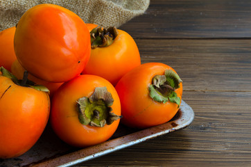 Fresh organic persimmon in vintage metal plate on rustic wood background. Concept for healthy food, vegan or raw diet.Copy space.