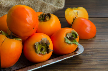 Fresh organic persimmon in vintage metal plate on rustic wood background. Concept for healthy food, vegan or raw diet.