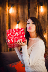 Attractive sensual young female with gift box sending a kiss over glittering background