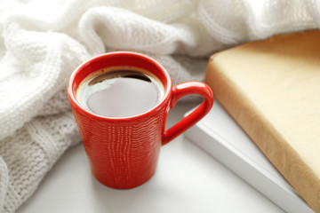 Fototapeta na wymiar Cup of fresh coffee with books and knitted plaid on windowsill