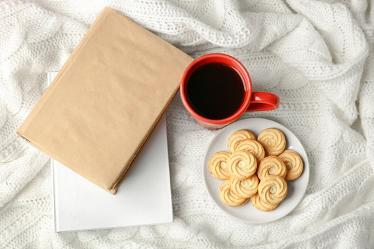 Cup of fresh coffee with biscuits  and books on knitted plaid, top view