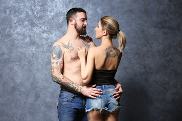 Passion tattooed beautiful couple on gray wall background