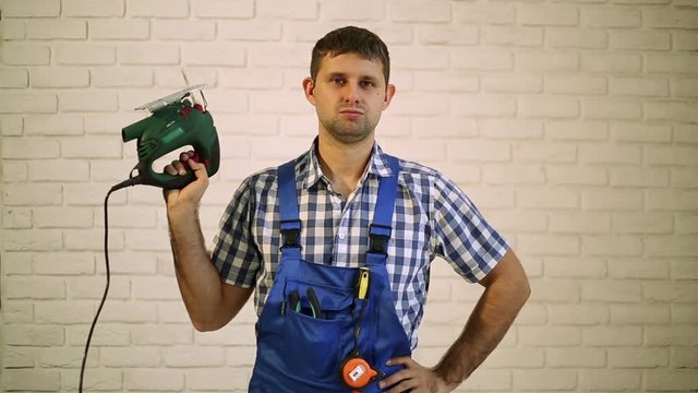 Man with an electric jigsaw. Work carpenter with an electric tool. Master, a professional repairman. Man holds in his hand an electric jigsaw.