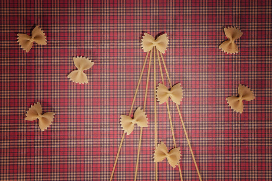 Christmas tree silhouette made of spaghetti and bow tie pasta on red squared background. Flat lay. Top view. Winter holidays concept