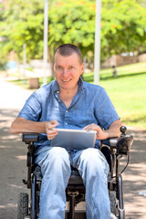Disabled man on wheelchair at the park holds tablet