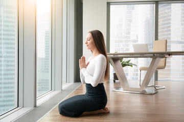 Young woman sitting on her feet knees together, office yoga, practicing seiza vajrasana pose to minimize discomfort of a desk work, making it easier to focus on work, relaxing after serious meeting