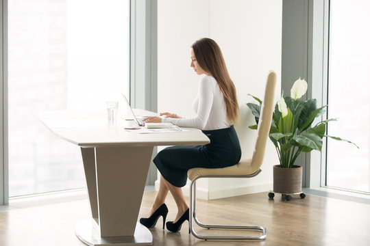Side view portrait of young woman in a formal wear working at the modern office desk, competent secretary, office etiquette, professional opportunities and rights for women, small office environment