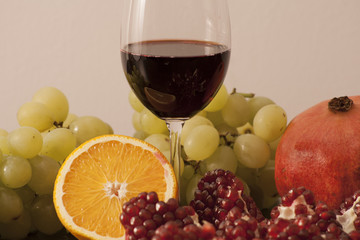 Glass of red wine and colorful fruits (pomegranate, orange, grapes)