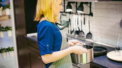 blonde woman with a pot in the kitchen. housewife in apron has been cooking in the kitchen, put pots and pans on the hob