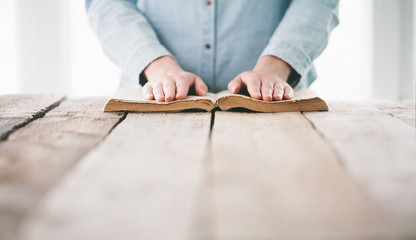 hands praying with a bible over wooden table