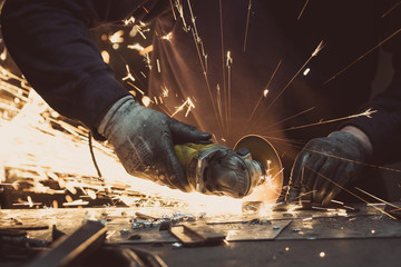 Man sawing metal with a rotary angle grinder on an aluminium surface and generating sparks - obrazy, fototapety, plakaty