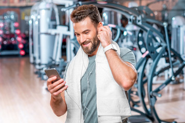 Lifestyle portrait of handsome smiling man standing with mobile phone after the training in the sport gym
