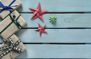 Cajas envueltas y decoradas para regalo, dos estrellas y un pino hechos de papel sobre una mesa pintada en azul. Imagen capturada con la suave luz de una ventana. Espacio para publicidad.