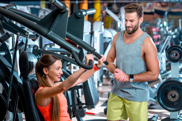 Fototapeta premium Young woman with personal trainer exercising on the simulator in the gym. Sport couple training together