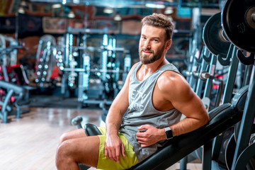 Fototapeta na wymiar Lifestyle portrait of handsome muscular man sitting on the simulator in the gym