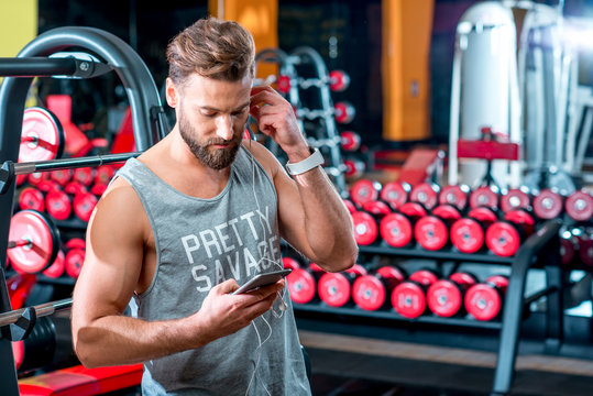 Man using smartphone standing in the gym after the training with red dumbbells on the background