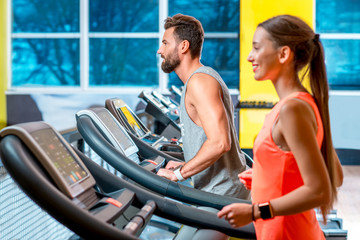Young sports couple making cardio workout on stationary treadmill in the gym.