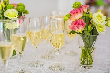 closeup glasses with champagne standing on the table, near the a vase of flowers