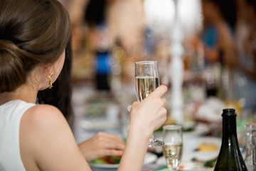 A girl holding a glass of champagne in hand. Festive evening in the restaurant.